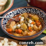 A bowl of vibrant Vegetable Chileajo Soup topped with fresh herbs.