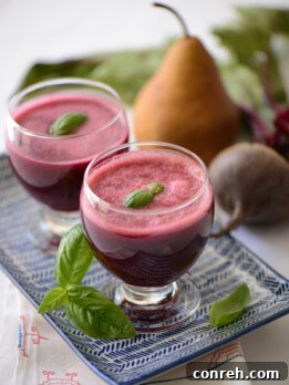 Vibrant red beet, pear, and basil juice in a glass with ingredients nearby