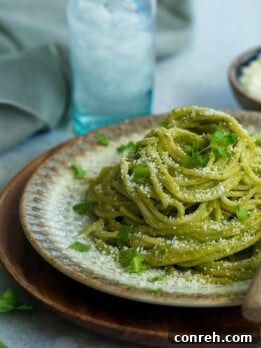 A plate of green creamy pasta garnished with crumbled white cheese and fresh cilantro.