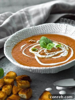 A bowl of vibrant red tomato soup with a swirl of cream and fresh basil