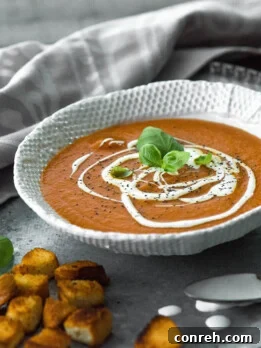 A comforting bowl of homemade tomato soup, garnished with fresh basil and a swirl of cream, ready to be enjoyed.