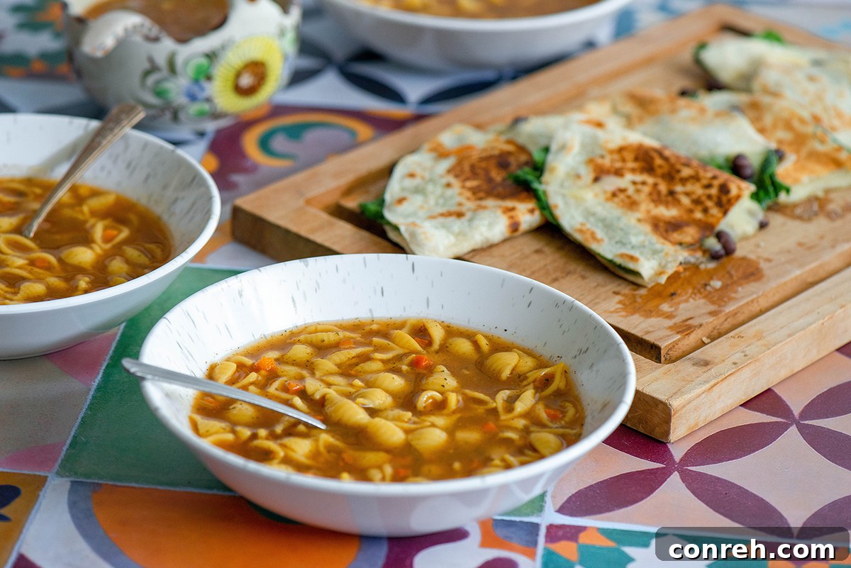A close-up of a spinach and black bean quesadilla, sliced in half, next to a bowl of soup.