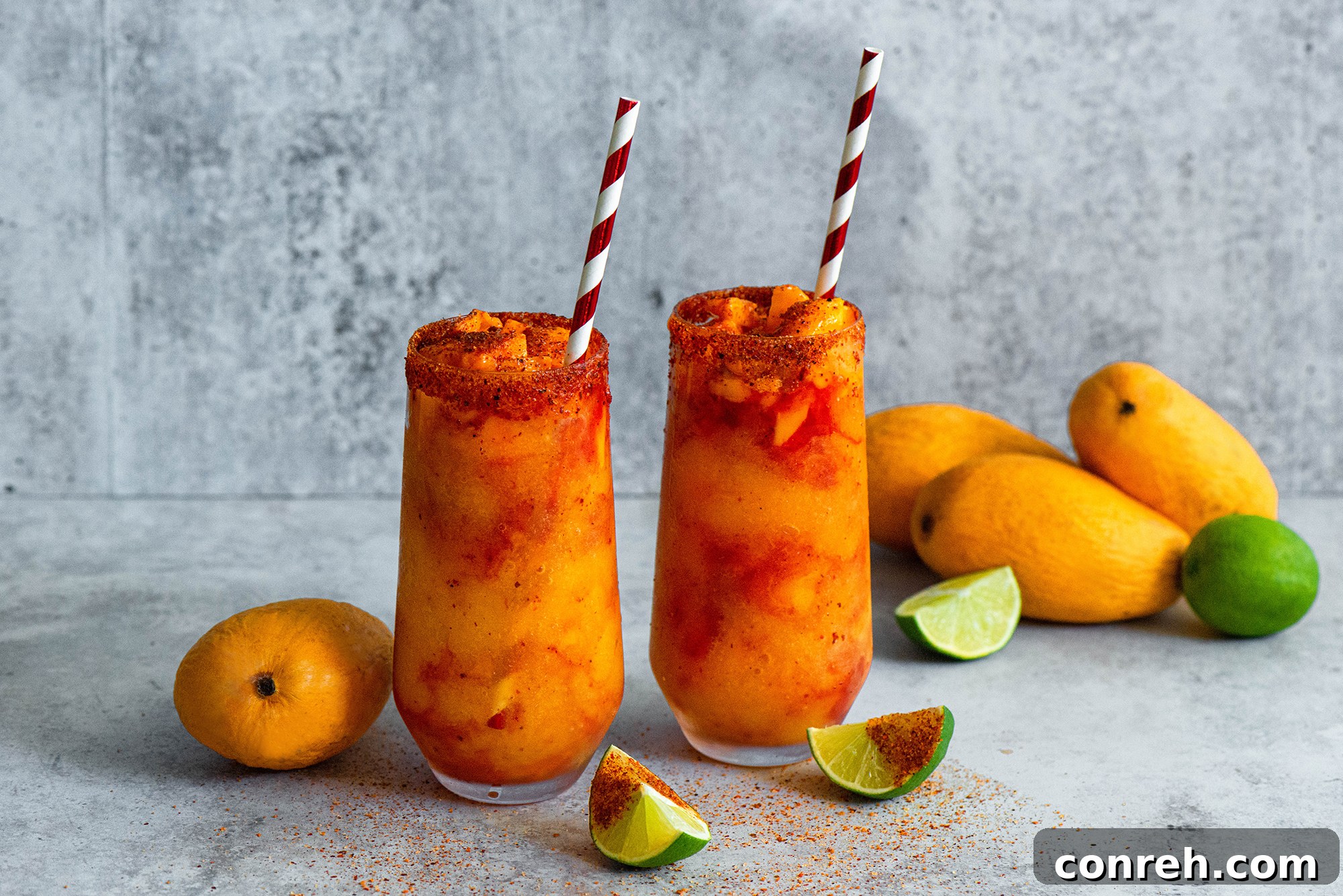 Two Mangonadas in tall glasses, with a focus on the layers of mango, chamoy, and fresh mango chunks, ready to be enjoyed.
