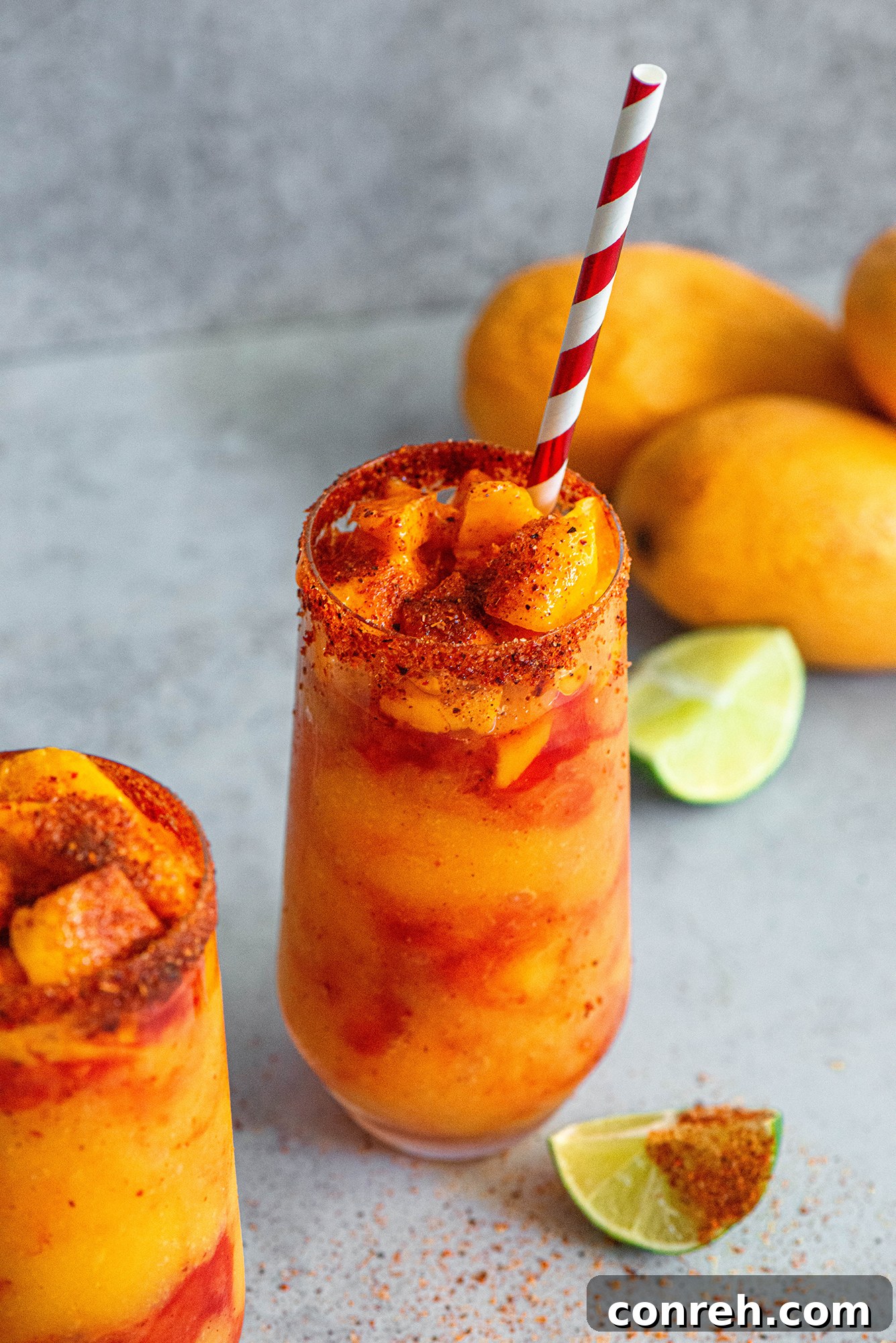 A close-up of a Mangonada, showing the bright orange mango blend, the dark red chamoy swirls, and the chili-lime salt rim.