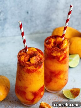 A perfectly prepared Mangonada, garnished with fresh mango chunks, tamarind candy straws, and a chili-lime salt rim.