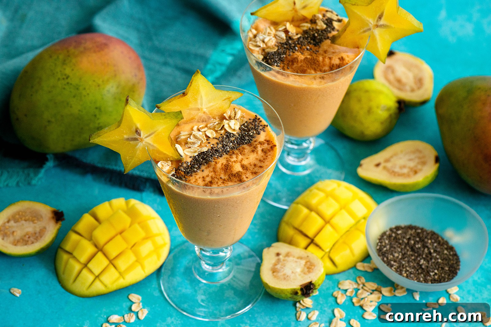Two glasses of Mango Guava Smoothie, garnished with star fruit slices and a sprinkle of cinnamon, sitting on a rustic wooden surface.