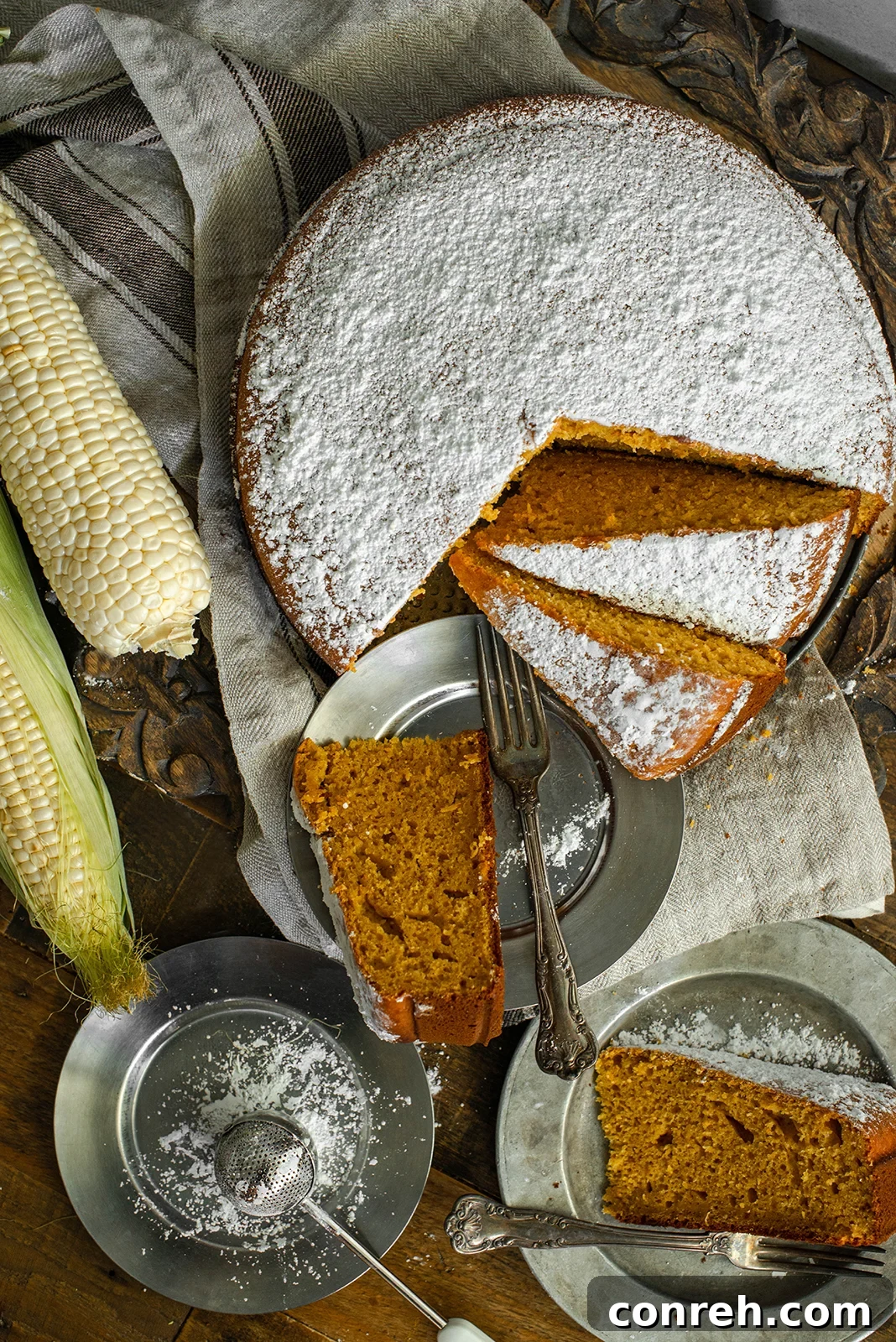 A slice of Pumpkin Corn Cake on a white plate, garnished with powdered sugar, next to a whole cake, showcasing its rich texture and autumn colors.