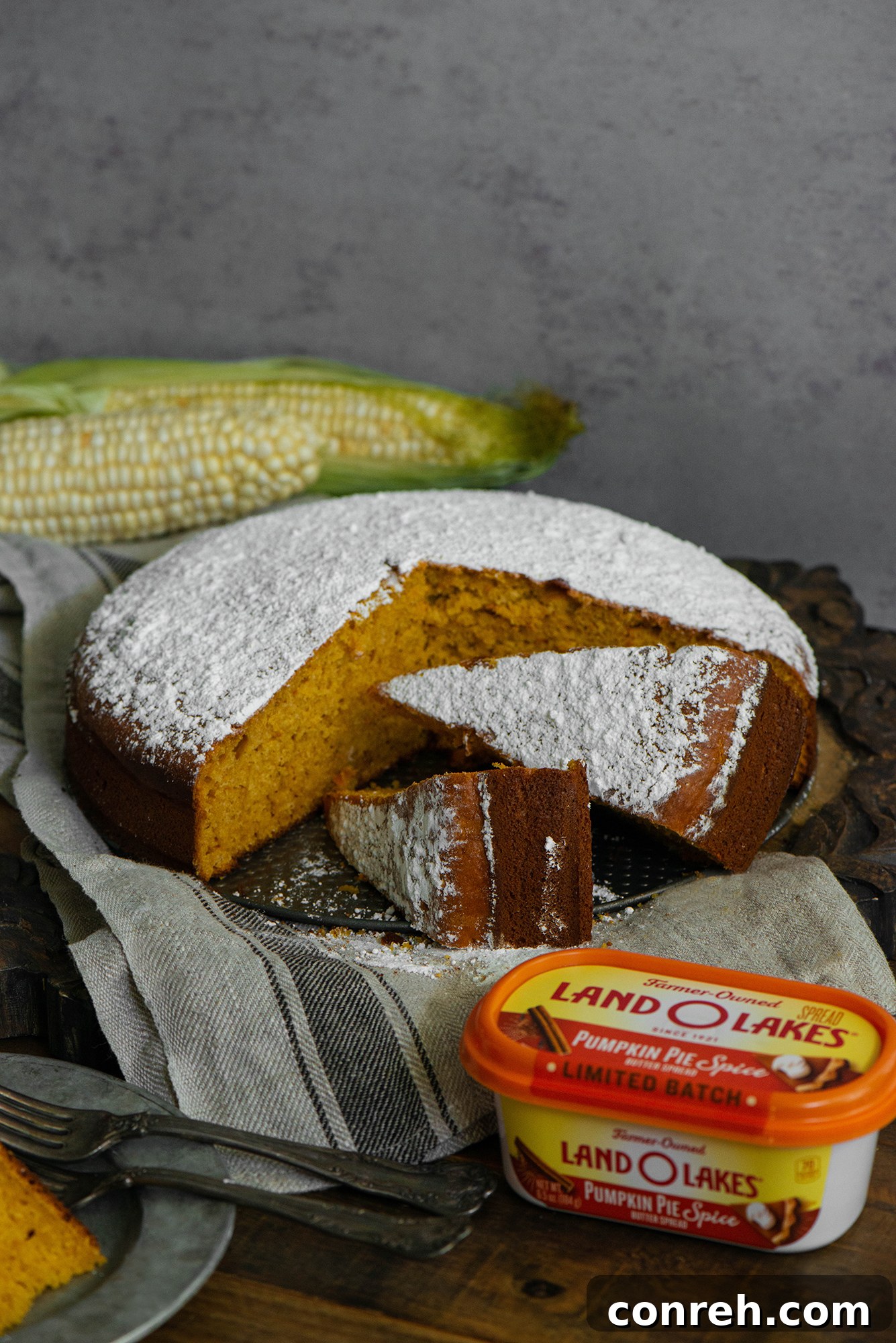 A beautifully presented whole Pumpkin Corn Cake, dusted with powdered sugar, ready for serving on a rustic wooden surface.