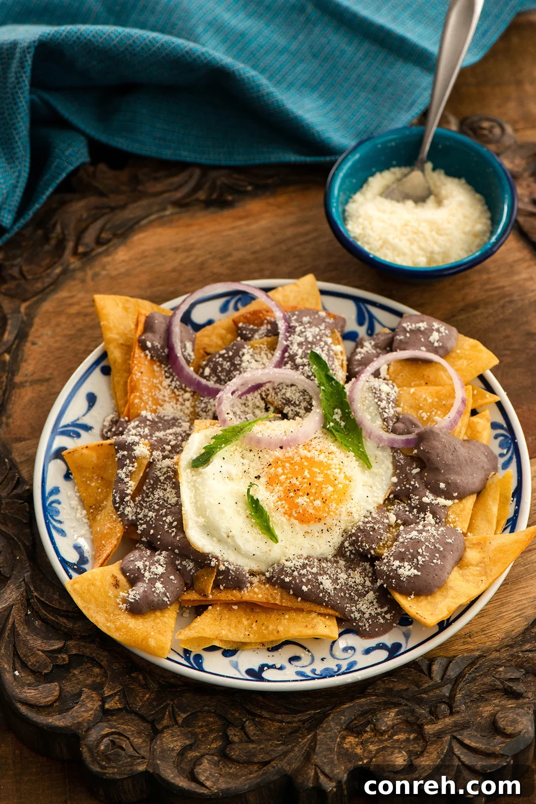 A vibrant plate of Black Bean Chilaquiles with a sunny-side up egg, crumbled cotija cheese, and fresh red onion slices.