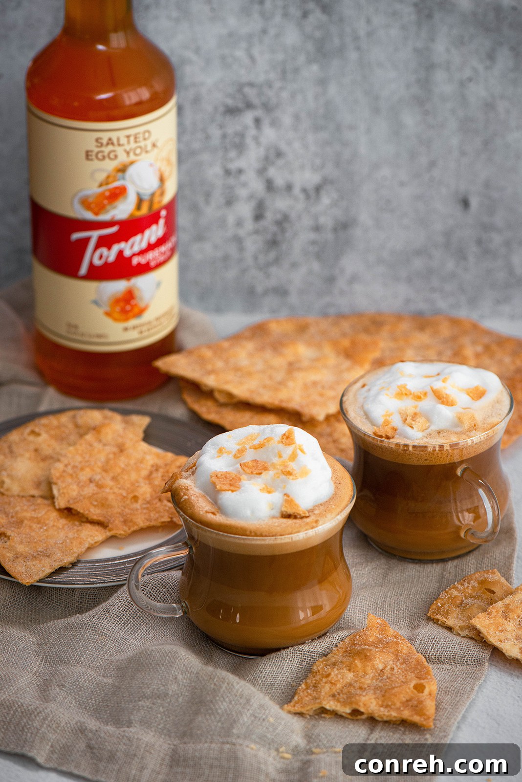 A bottle of Torani Puremade Salted Egg Yolk Syrup next to a beautifully prepared Salted Egg Yolk Latte, highlighting the product and its use.
