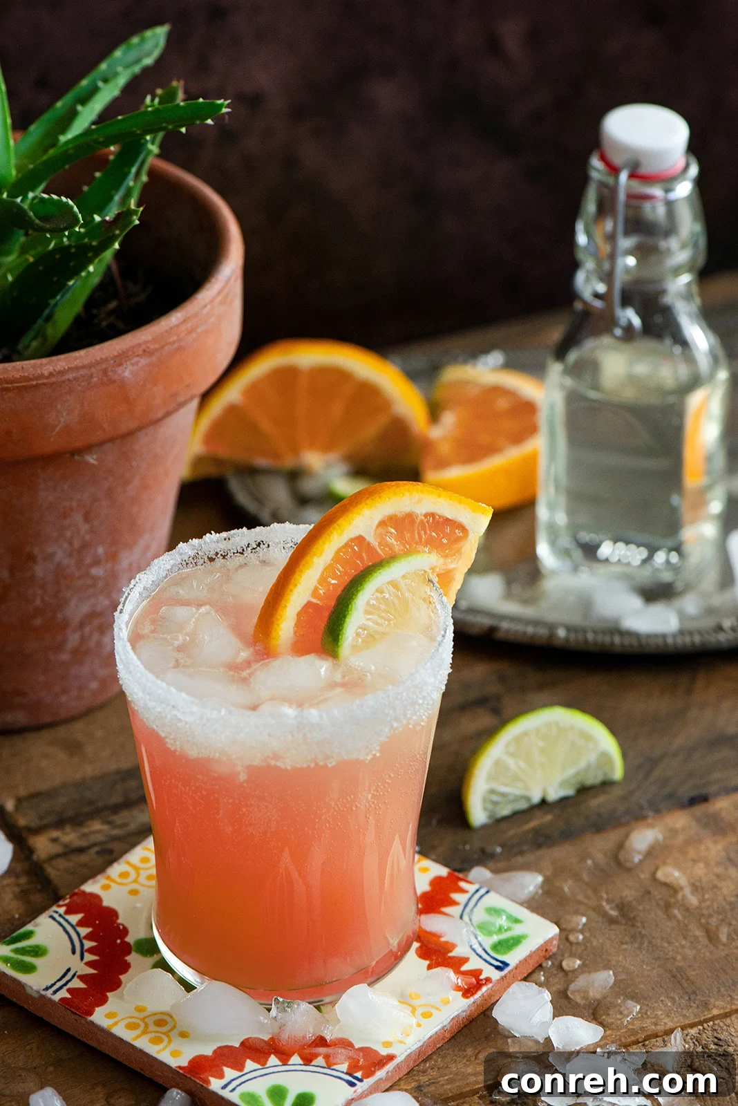 A refreshing Paloma cocktail garnished with a grapefruit slice and lime wedge, sitting on a wooden surface.