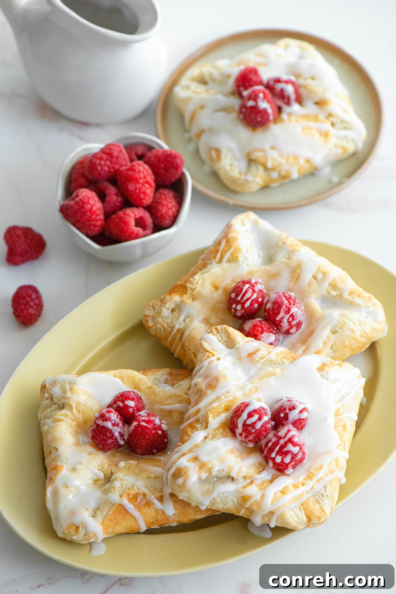 A stack of freshly baked cheese danishes with fresh raspberries on top, presented beautifully.