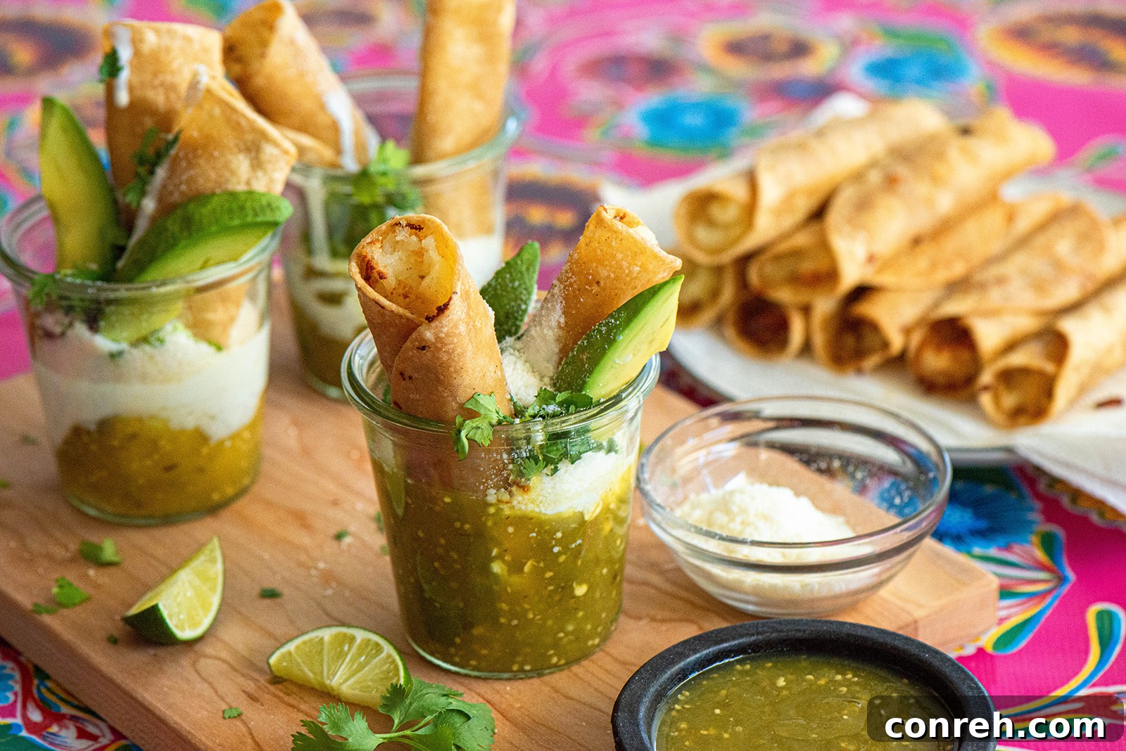 Two hands holding a cup of Taquitos Ahogados, showcasing the vibrant green salsa, white crema, and crumbled cheese.