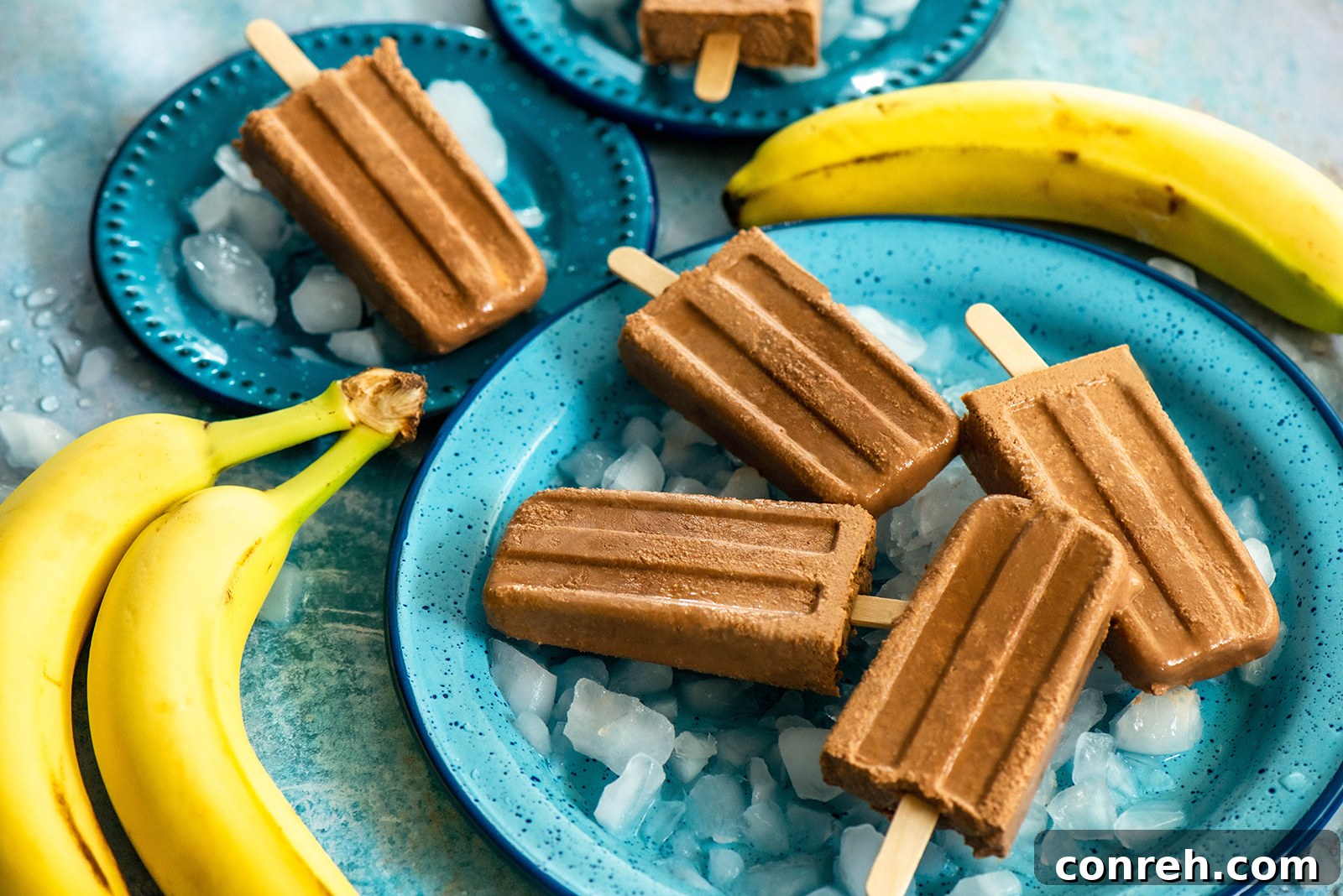 A selection of ripe bananas with brown spots, unsweetened cocoa powder, and a container of heavy cream, key ingredients for homemade popsicles.