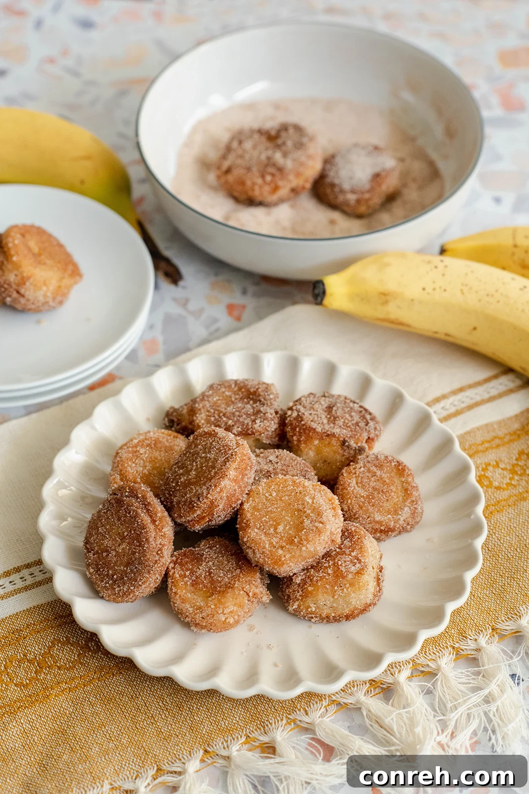 Close-up of golden brown battered banana bites coated in cinnamon sugar, served on a plate.