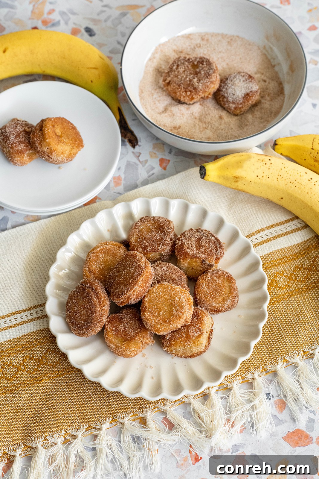 A close-up shot of a stack of golden battered banana bites, generously coated in cinnamon sugar, on a rustic wooden surface.