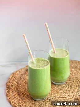 Green Goddess Smoothie in a glass with a straw and a few pieces of spinach