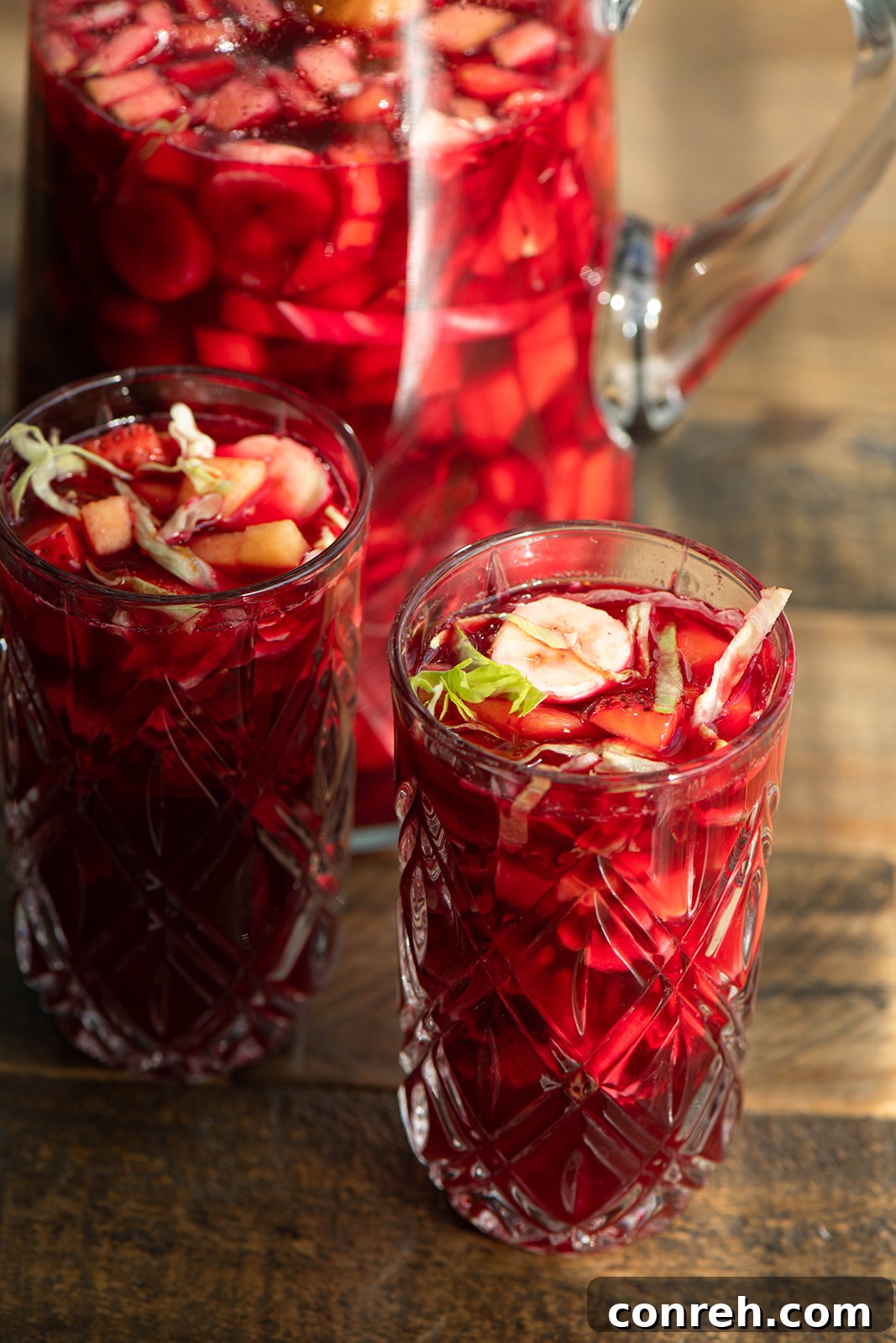 Close-up of a glass of Agua de Cuaresma, showcasing the diced fruits and shredded lettuce suspended in the beet-infused red liquid.