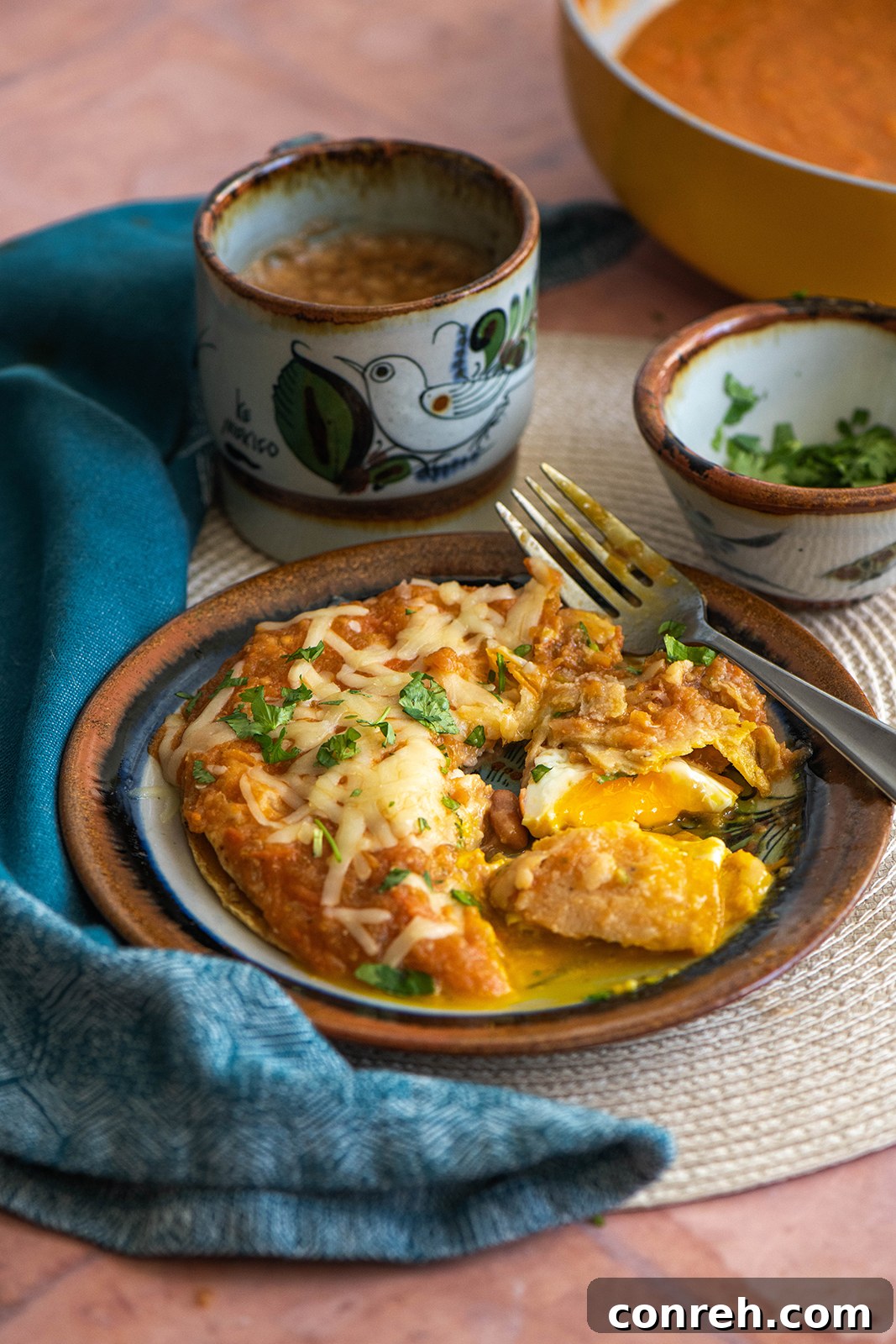 Close-up of Huevos Encobijados with melted cheese and fresh cilantro, showcasing the rich tomato sauce and tortillas.