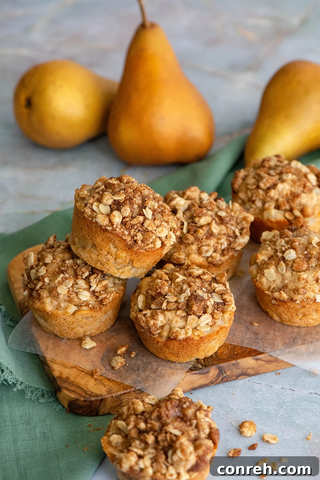 A beautifully styled flat lay of two oat pear muffins on a dark surface, one with a bite taken out, surrounded by fresh pears and oats, creating a rustic autumn scene.