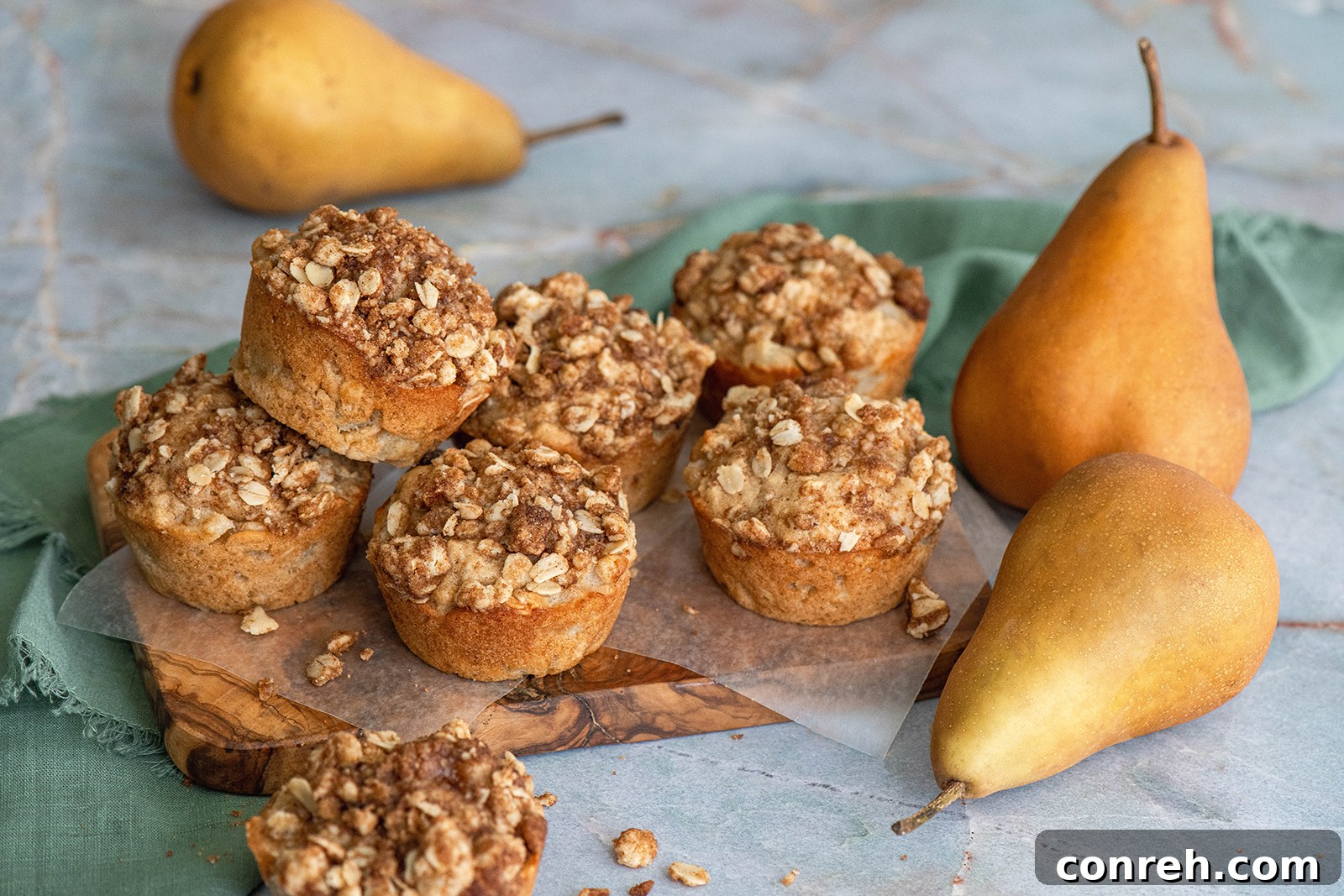 A close-up, top-down shot of several golden-brown oat pear streusel muffins arranged on a rustic wooden board, showing their inviting crumbly tops and warm color.