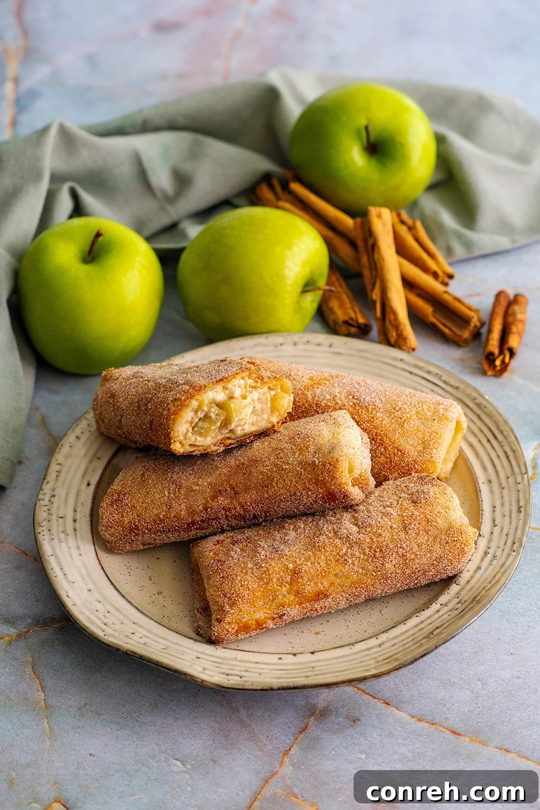 Crispy golden apple cheesecake chimichangas arranged beautifully on a plate, dusted with cinnamon sugar