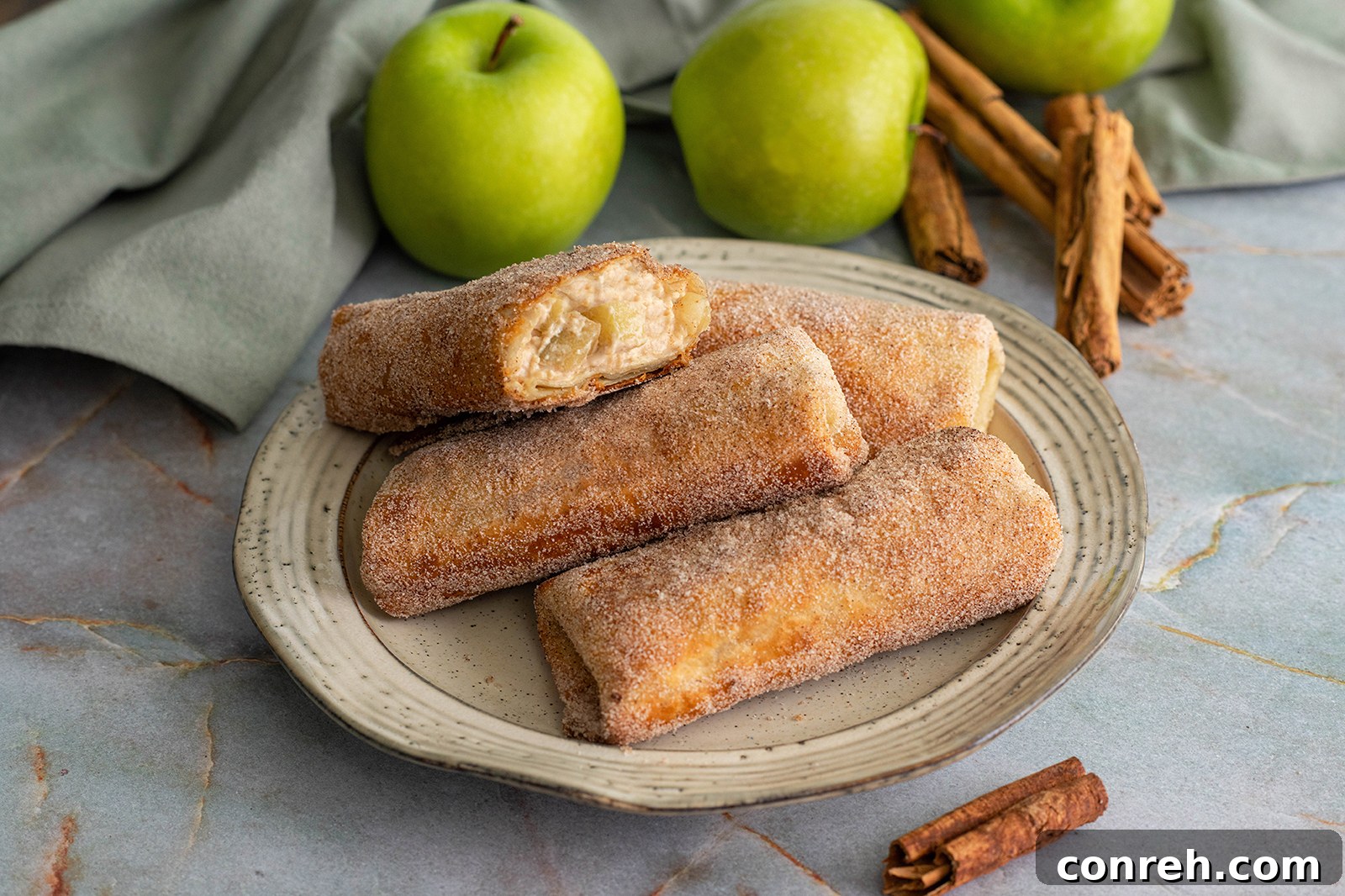 Close-up of a perfectly rolled and fried apple cheesecake chimichanga dusted with cinnamon sugar, ready to be enjoyed