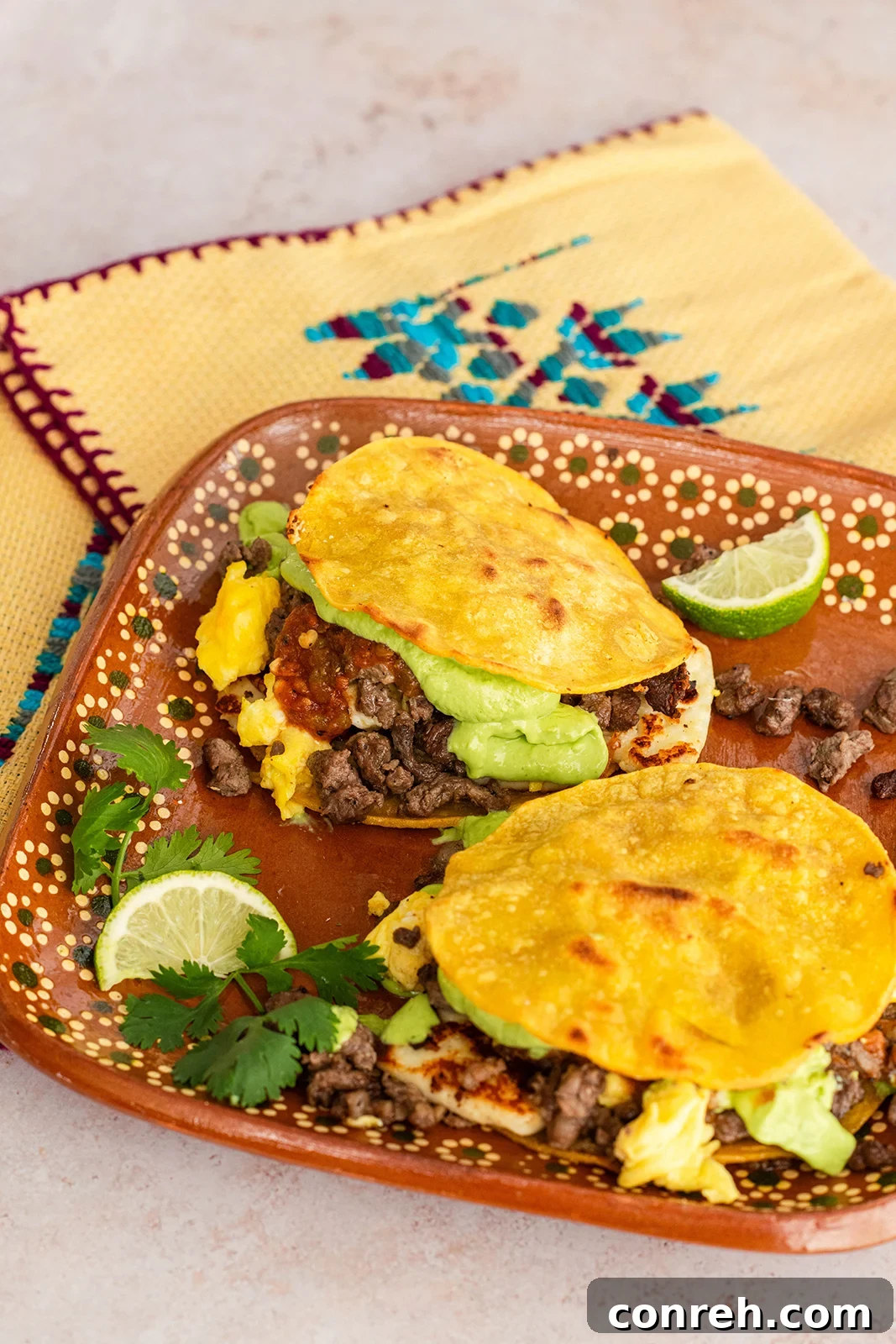 A close-up of delicious breakfast mulitas, garnished with fresh cilantro and a dollop of avocado crema, showcasing the vibrant fillings.