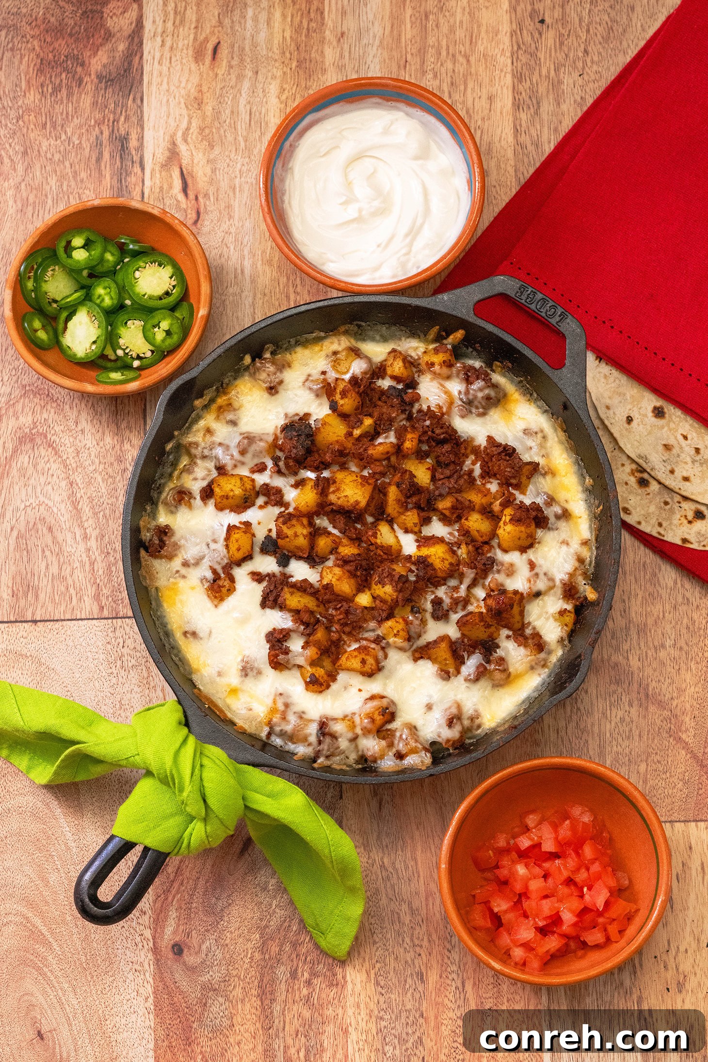 A vibrant skillet of Potatoes & Chorizo Queso Fundido, with melted Oaxaca cheese, savory chorizo, and tender potatoes, garnished with fresh cilantro and served with warm tortillas.