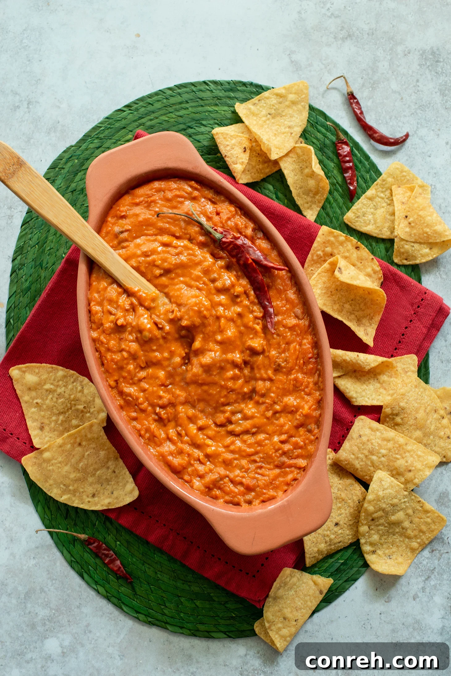 A vibrant bowl of Frijoles Maneados, rich and cheesy Mexican stirred beans, garnished with fresh cilantro and served with warm tortillas and crispy tortilla chips on a rustic wooden surface.