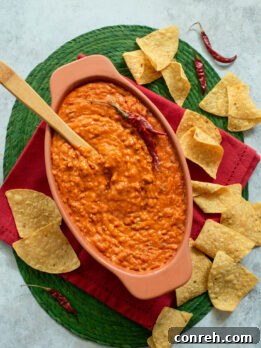 A close-up shot of Frijoles Maneados served in a vibrant, decorative bowl, highlighting the melted cheese and creamy texture, ready to be enjoyed with a side of crispy tortilla chips.