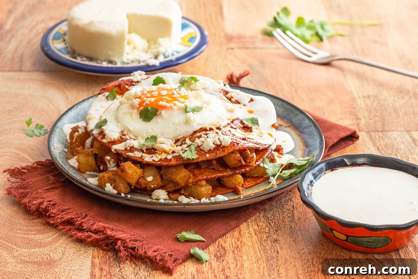 Close-up of golden brown stacked enchiladas with a fried egg and crema.