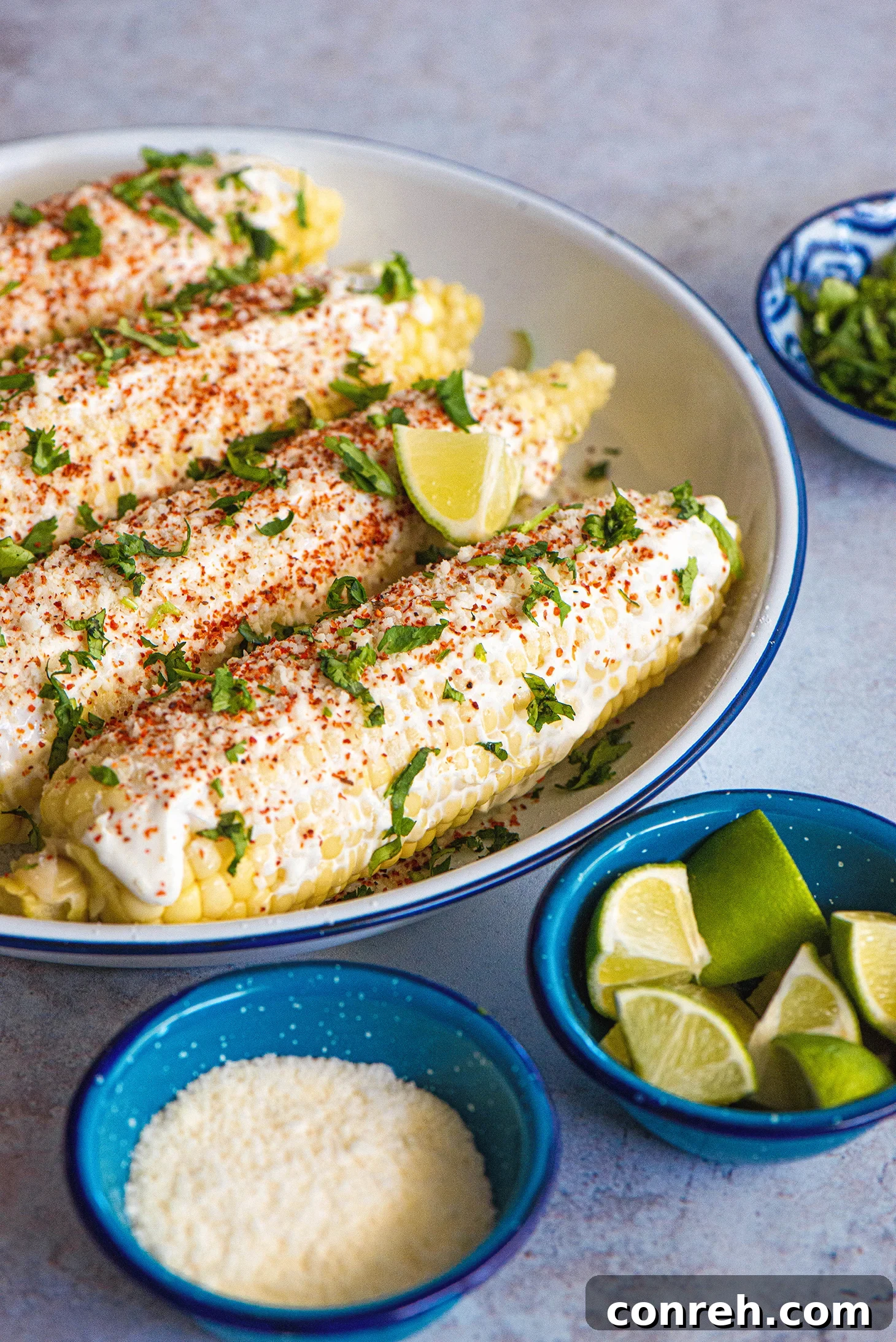 A close-up of a prepared elote with mayonnaise, cheese, chili, and cilantro.