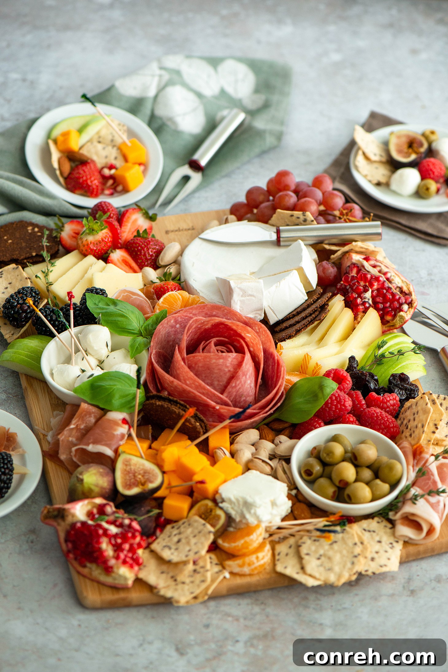 Hand arranging various ingredients on a large wooden charcuterie board for summer entertaining