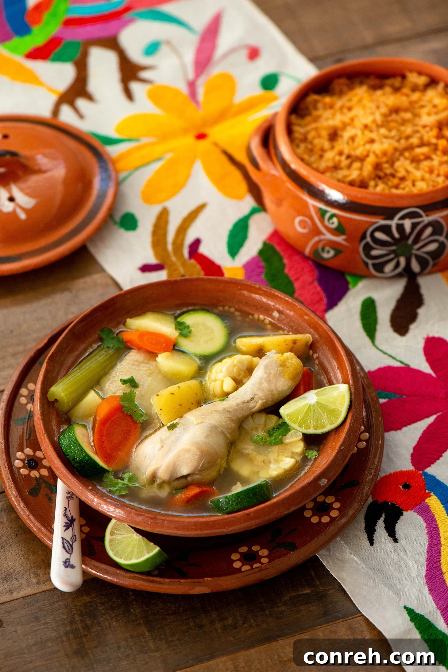 Steaming bowl of Caldo de Pollo, Mexican chicken soup with corn, carrots, and cilantro, served with lime wedges