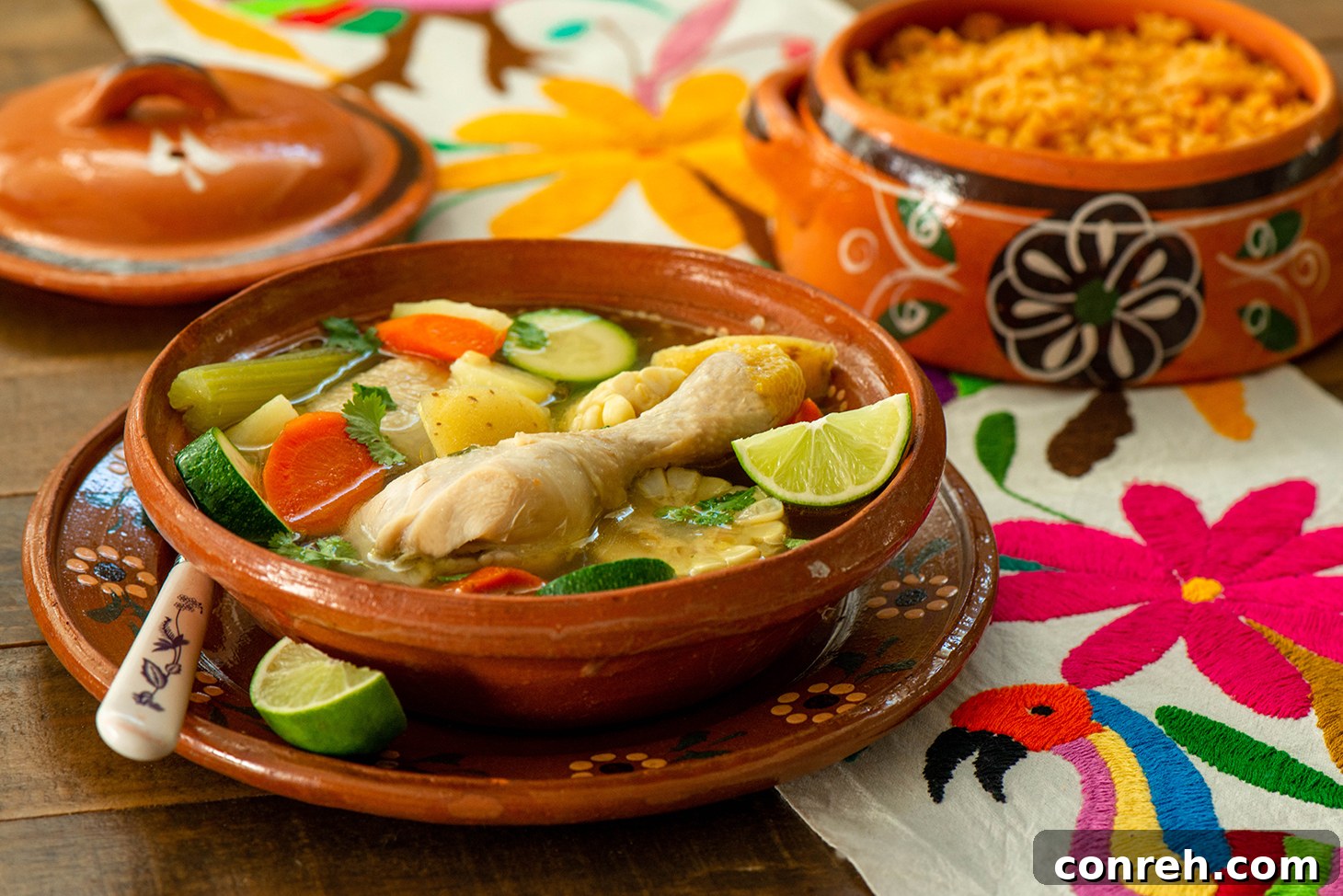 Close-up of a rustic bowl of Caldo de Pollo with fresh cilantro, a chicken drumstick, and lime wedges on the side