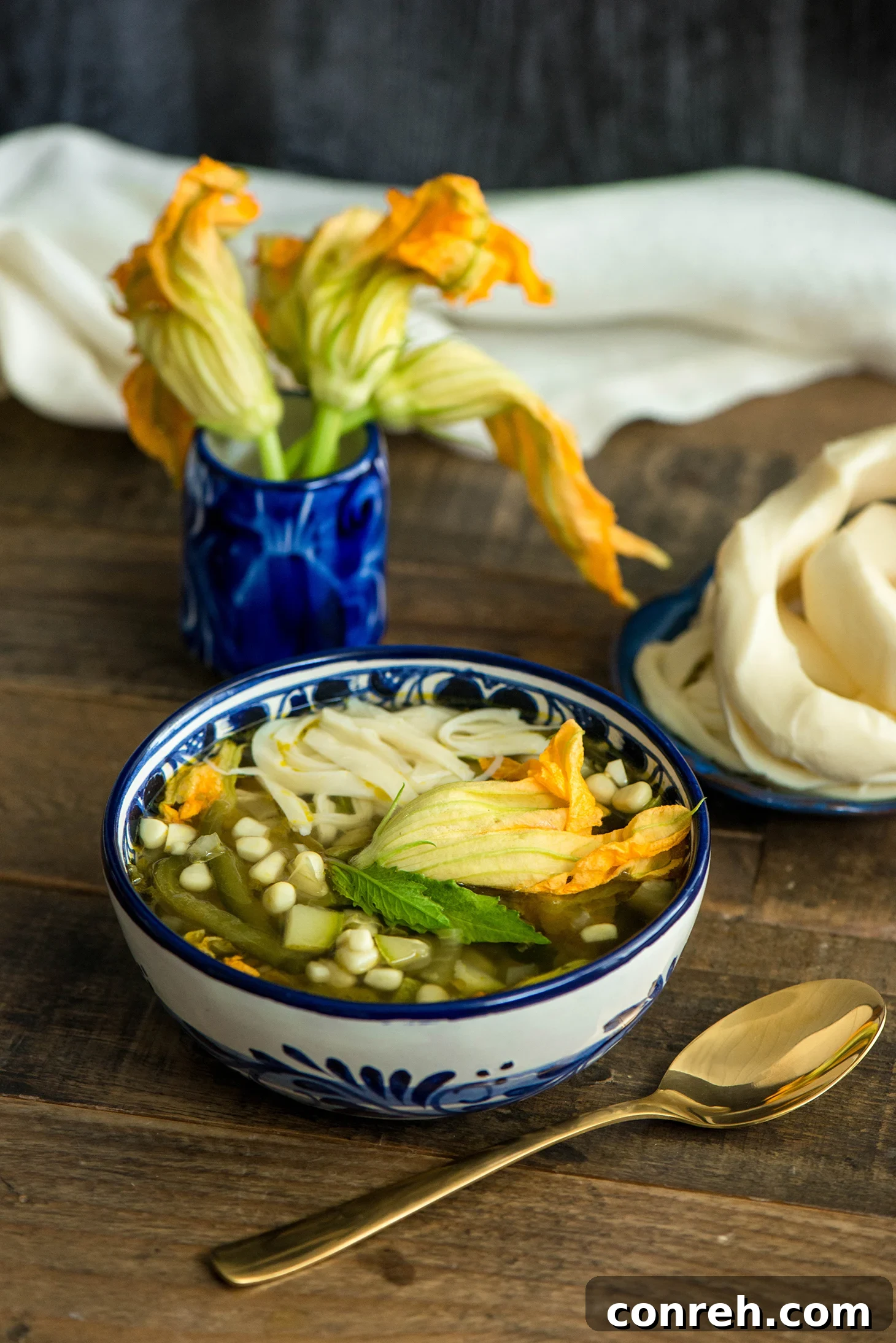 A vibrant bowl of Sopa de Milpa, showcasing fresh corn, squash blossoms, and herbs in a light broth.