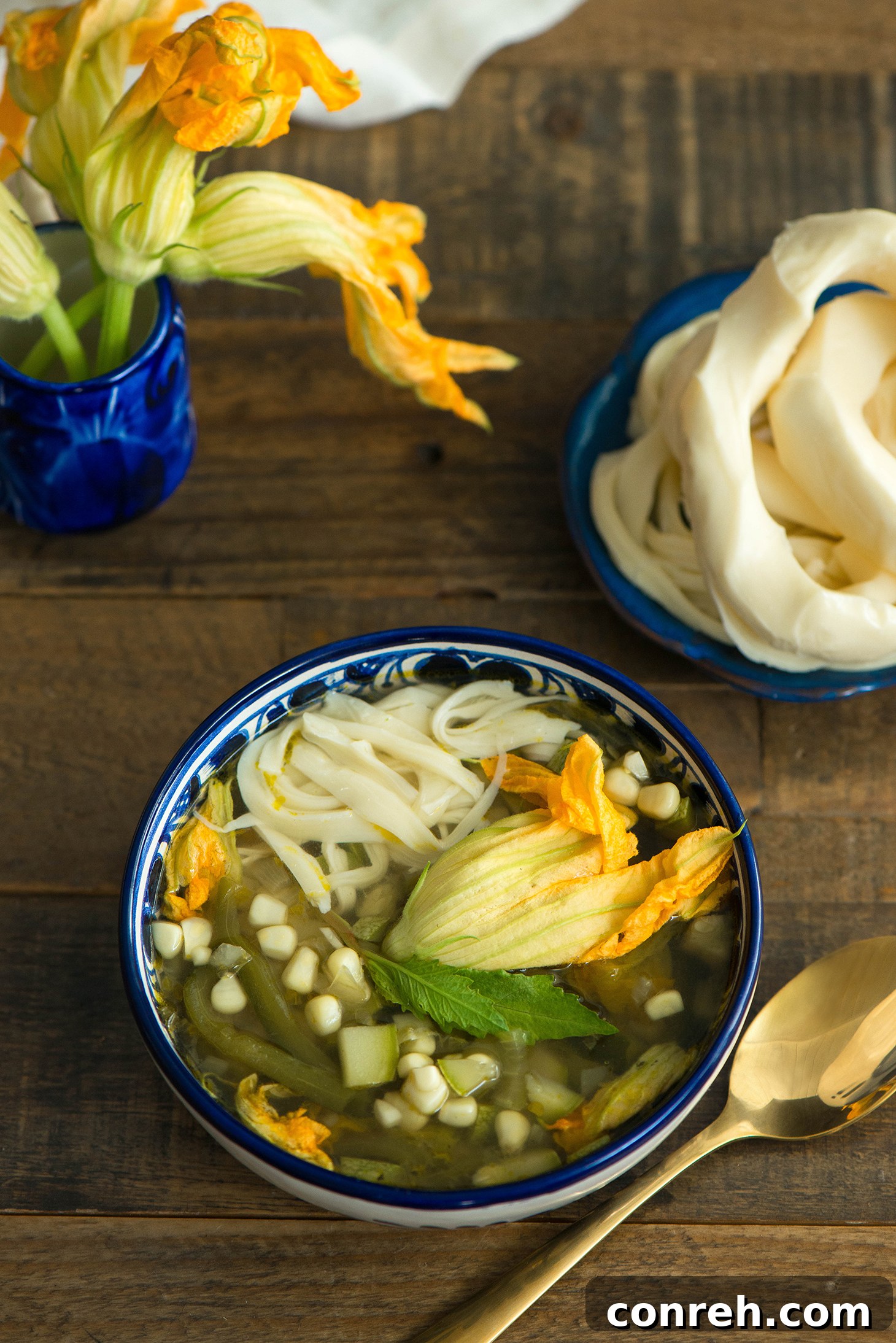 Overhead shot of a beautifully presented bowl of Sopa de Milpa, garnished with cheese and a spoon.