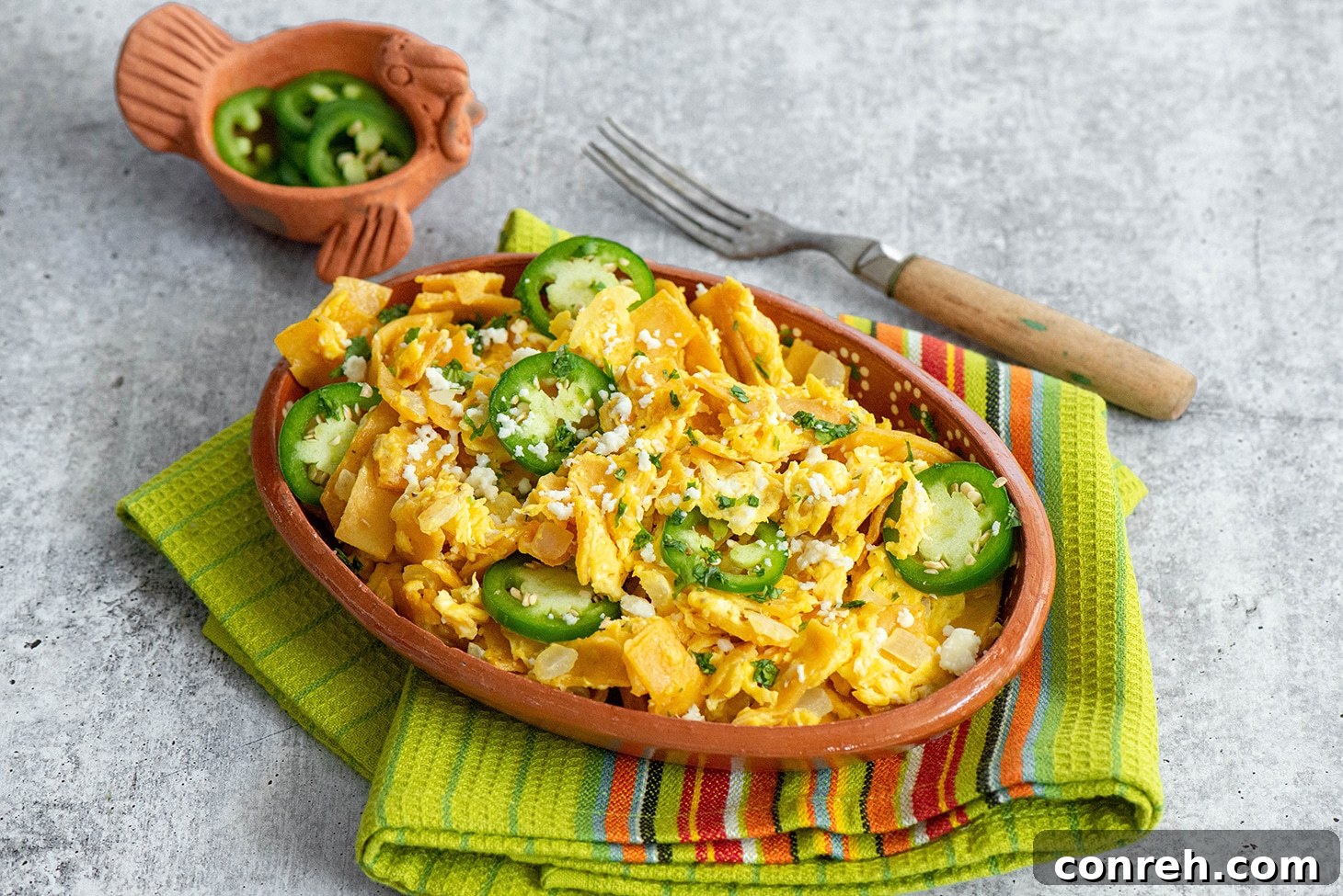 Close-up of Migas being prepared in a skillet, with tortillas and onions frying before eggs are added.