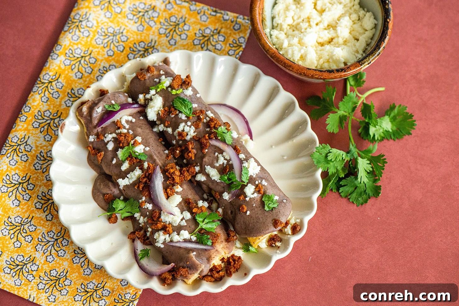Close-up of freshly prepared Enfrijoladas topped with crumbled queso fresco and red onion.