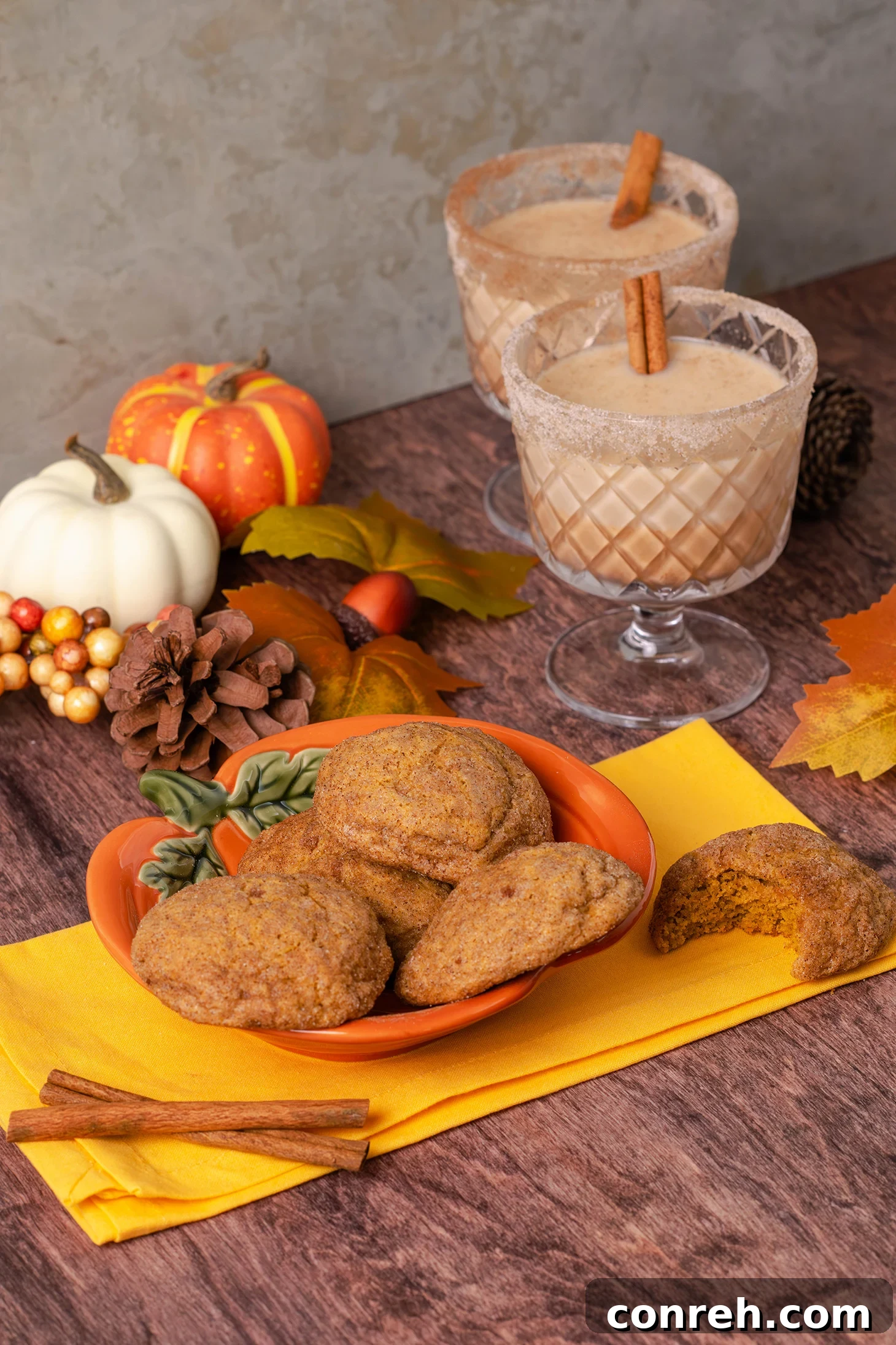 A close-up shot of several Pumpkin Churro Cookies, coated in cinnamon sugar, stacked on a rustic wooden surface with fall decorations in the background.