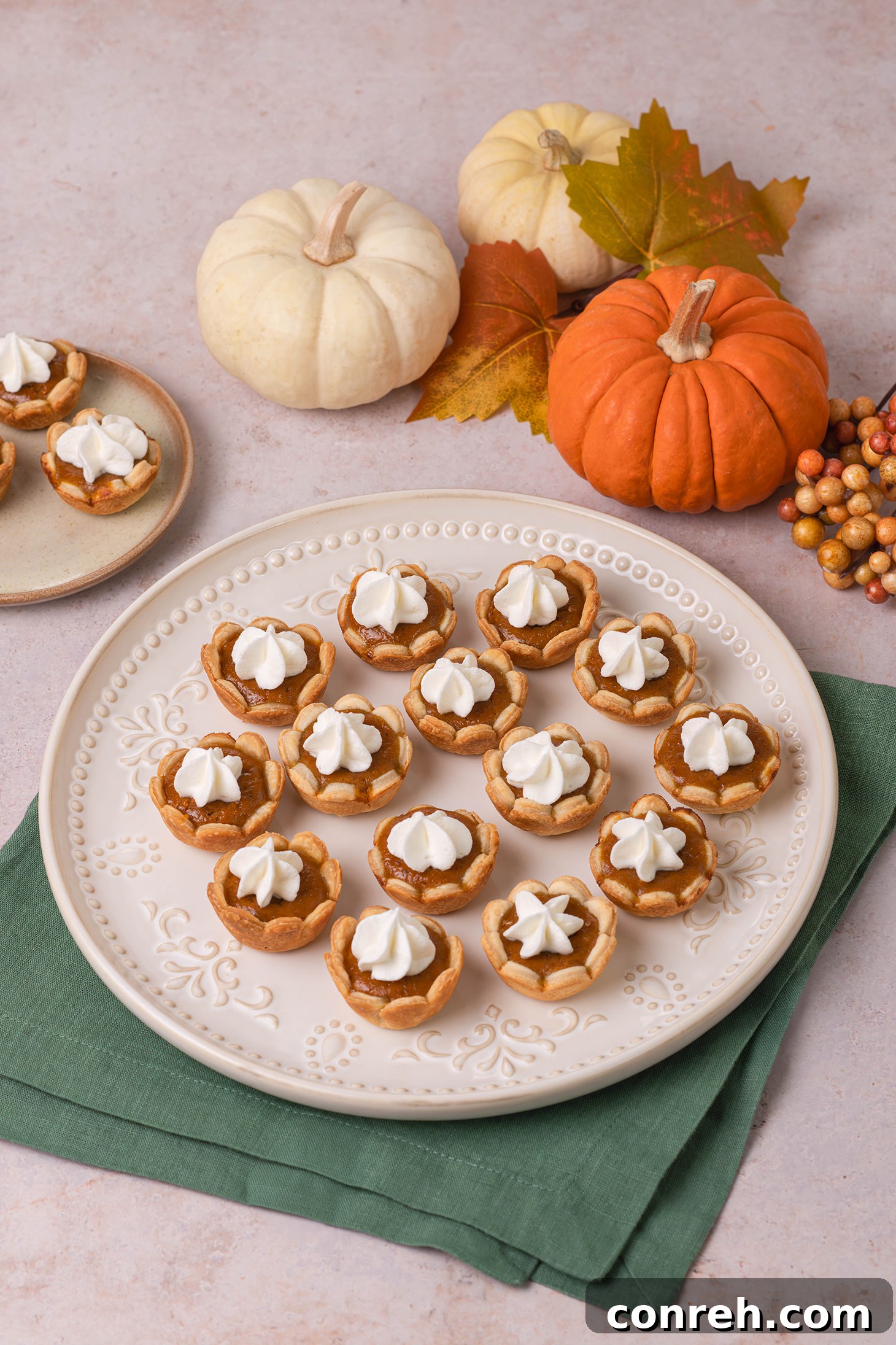 Close-up of a mini pumpkin pie with a crimped crust, garnished with whipped cream and a sprinkle of cinnamon.