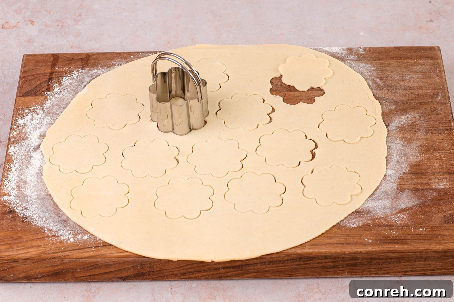 Using a flower-shaped cookie cutter on pie dough on a floured surface.