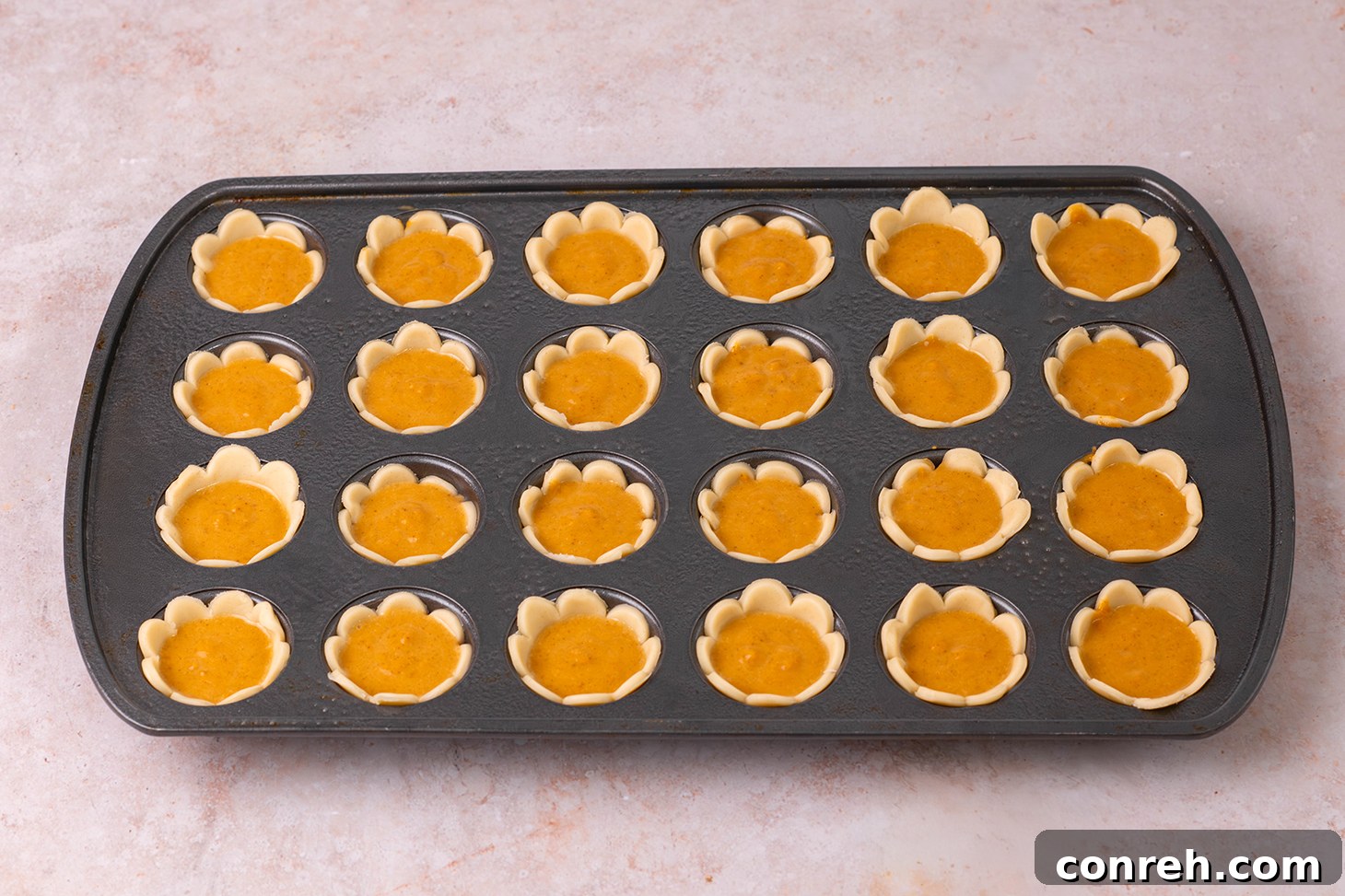Filling mini pie crusts in a muffin tin with pumpkin mixture.