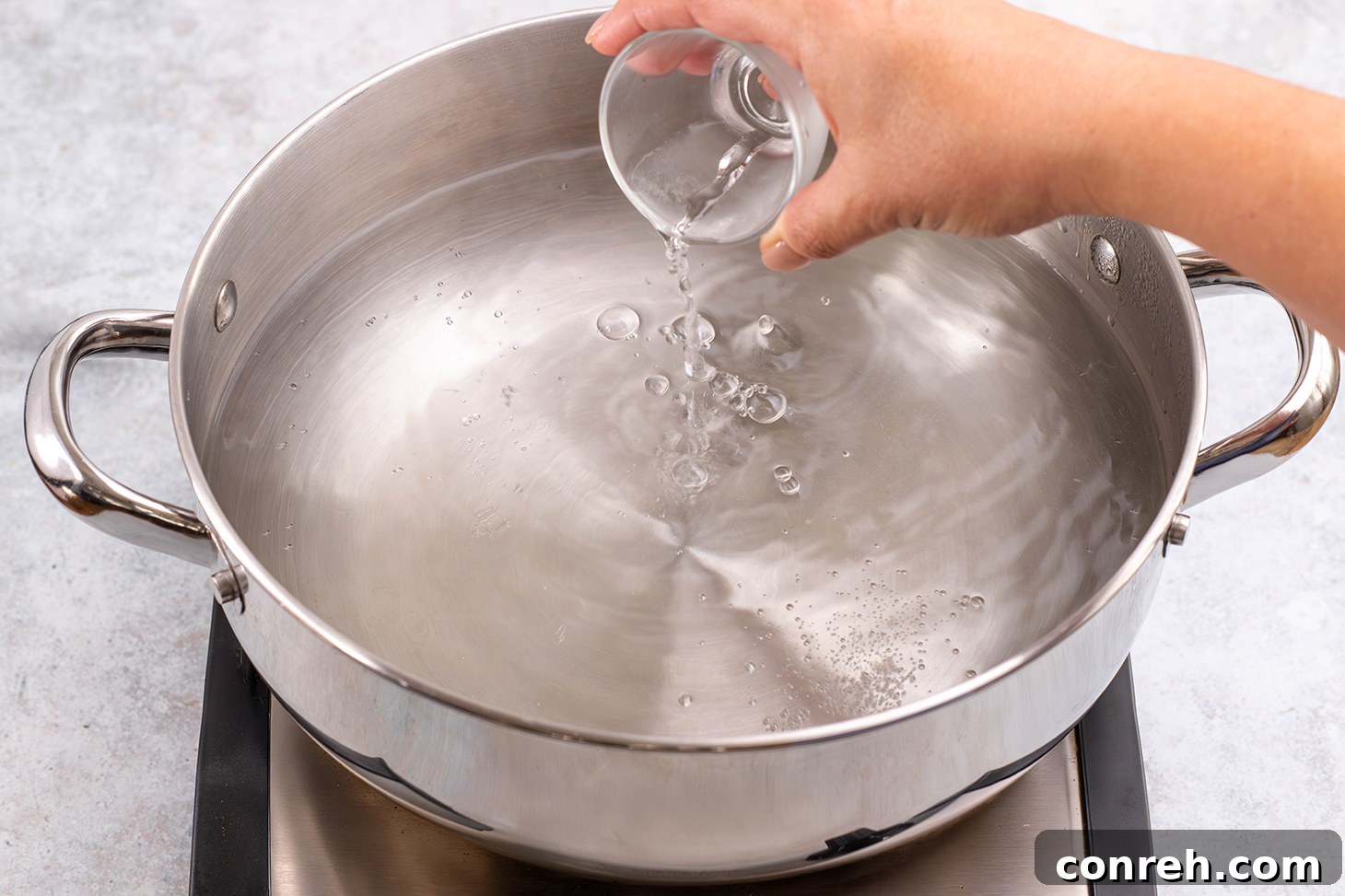 Adding white vinegar to simmering water in a saucepan.