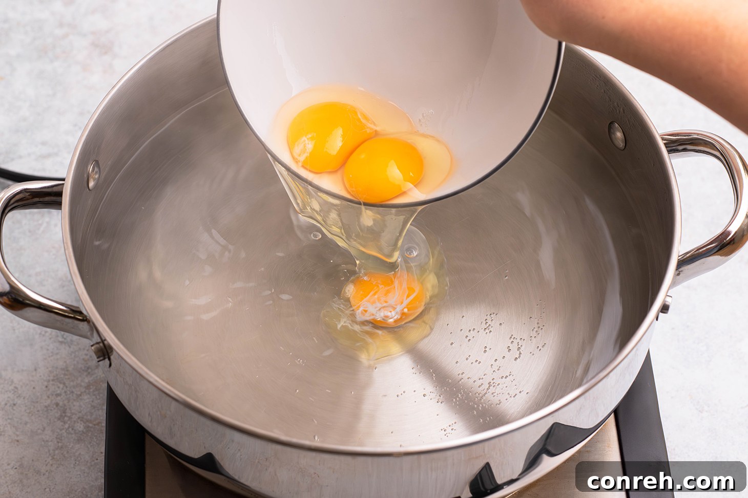 Gently lowering an egg from a ramekin into the center of the whirlpool.