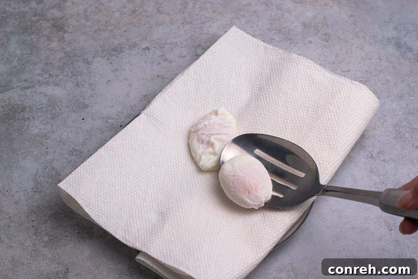 A freshly poached egg draining on a paper towel-lined plate.